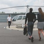 Young fashionable couple walking towards the pilot of a white private helicopter